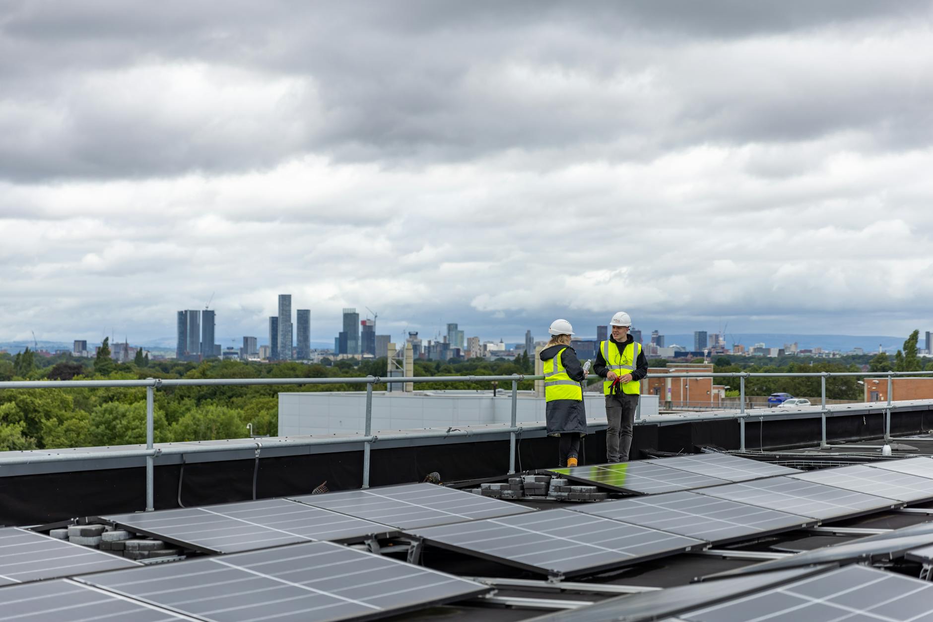 Two workers checking solar panels on a rooftop with a city skyline in the background.