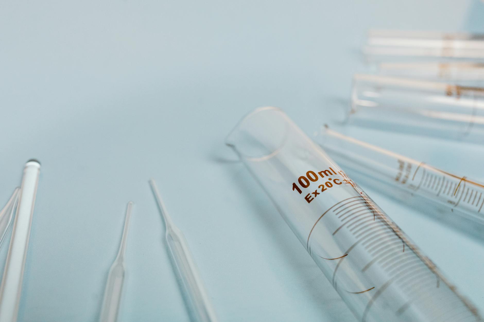 A collection of transparent glass test tubes on a soft blue surface, ideal for scientific research visuals.