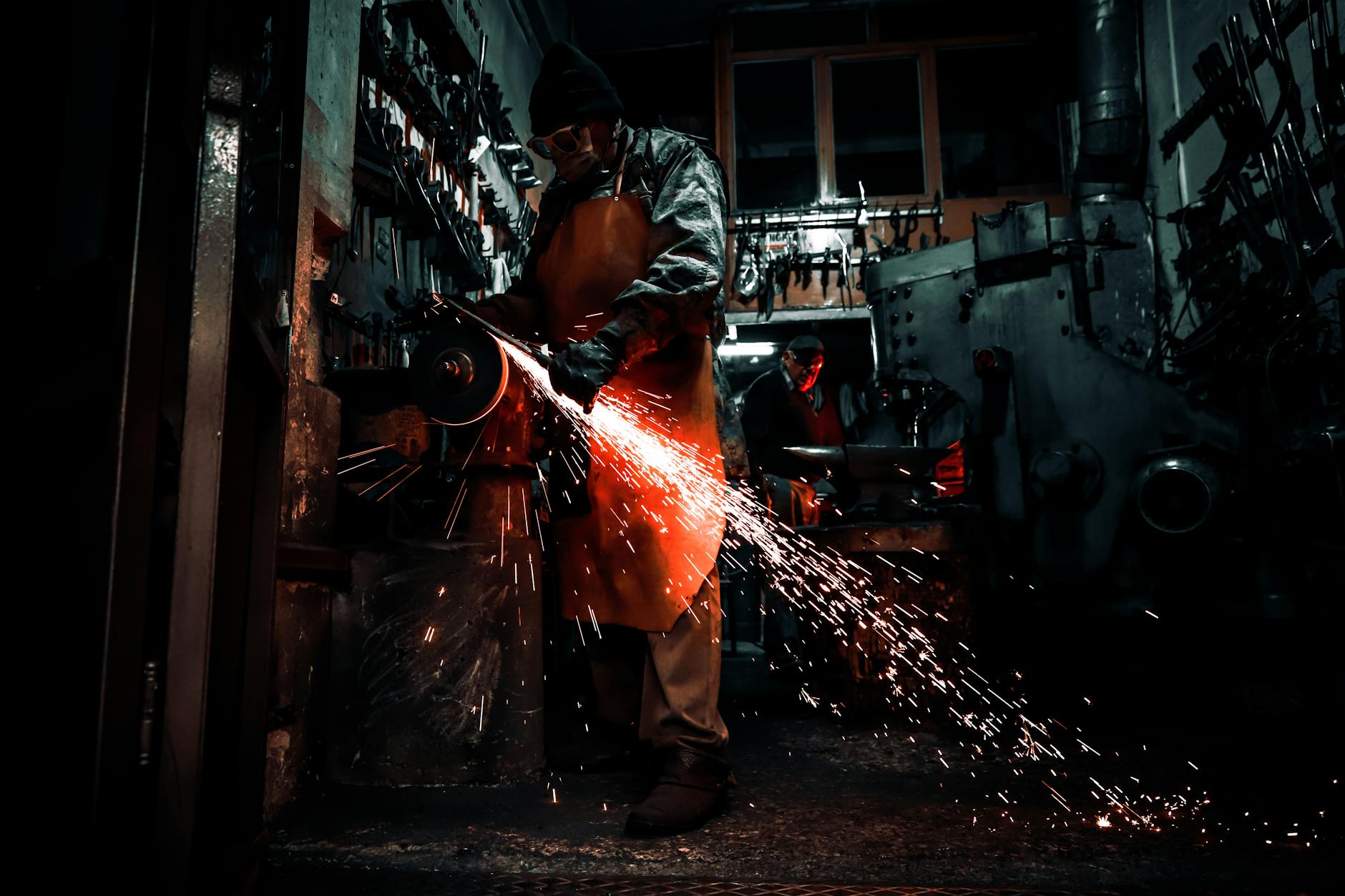 Metalworker using grinding machine in dimly lit workshop, sparks flying.